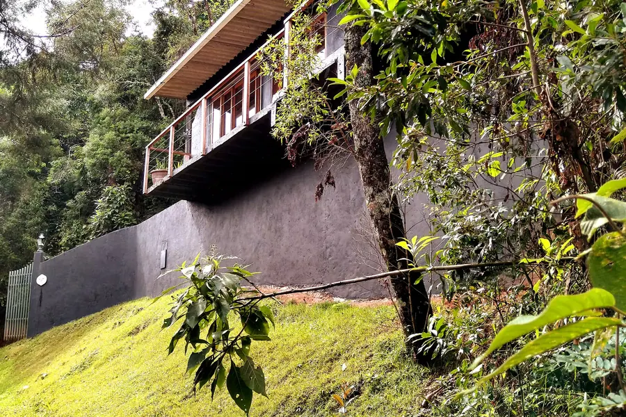 Fachada da Guttos House com varanda suspensa em madeira, cercada pela mata em Campos do Jordão