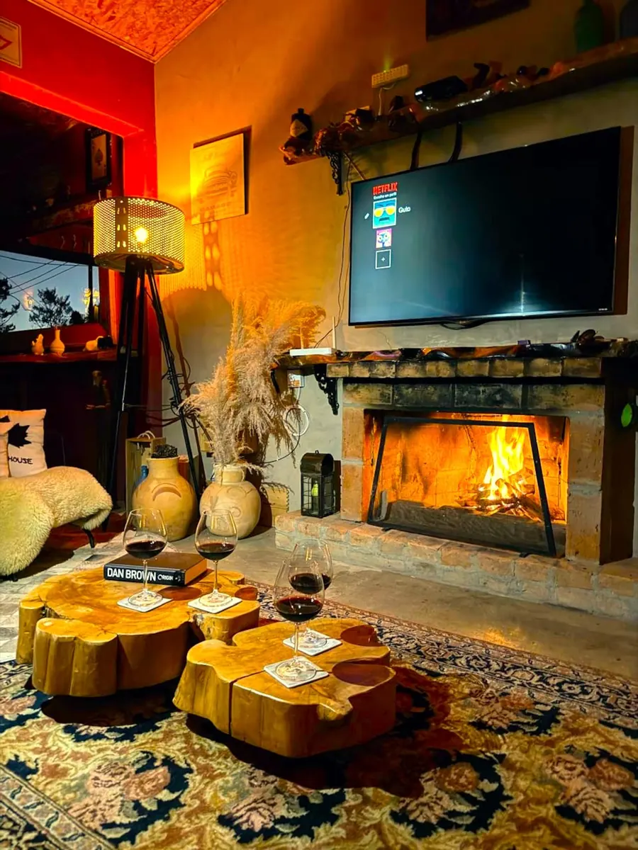 Lareira acesa à noite, taças de vinho sobre mesas de tronco e Smart TV na sala de estar