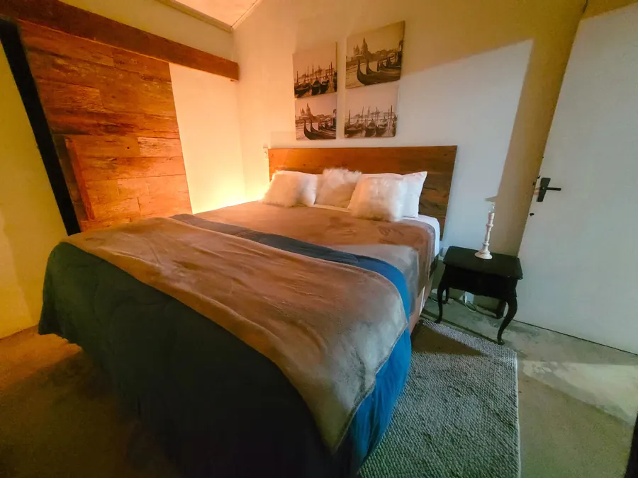 Quarto com cama arrumada, almofadas felpudas e parede de madeira de demolição