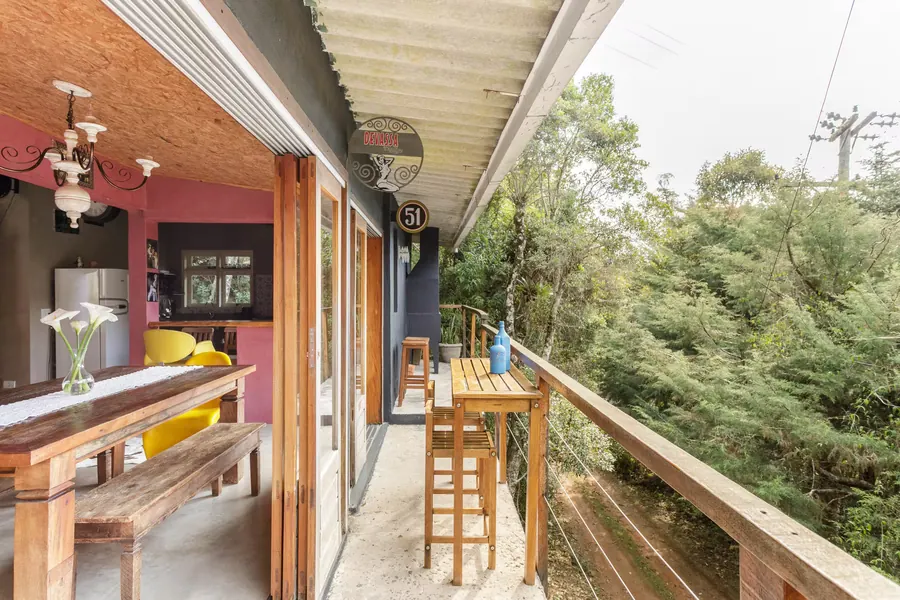 Varanda com mesa alta de madeira integrada à sala de jantar, voltada para a mata